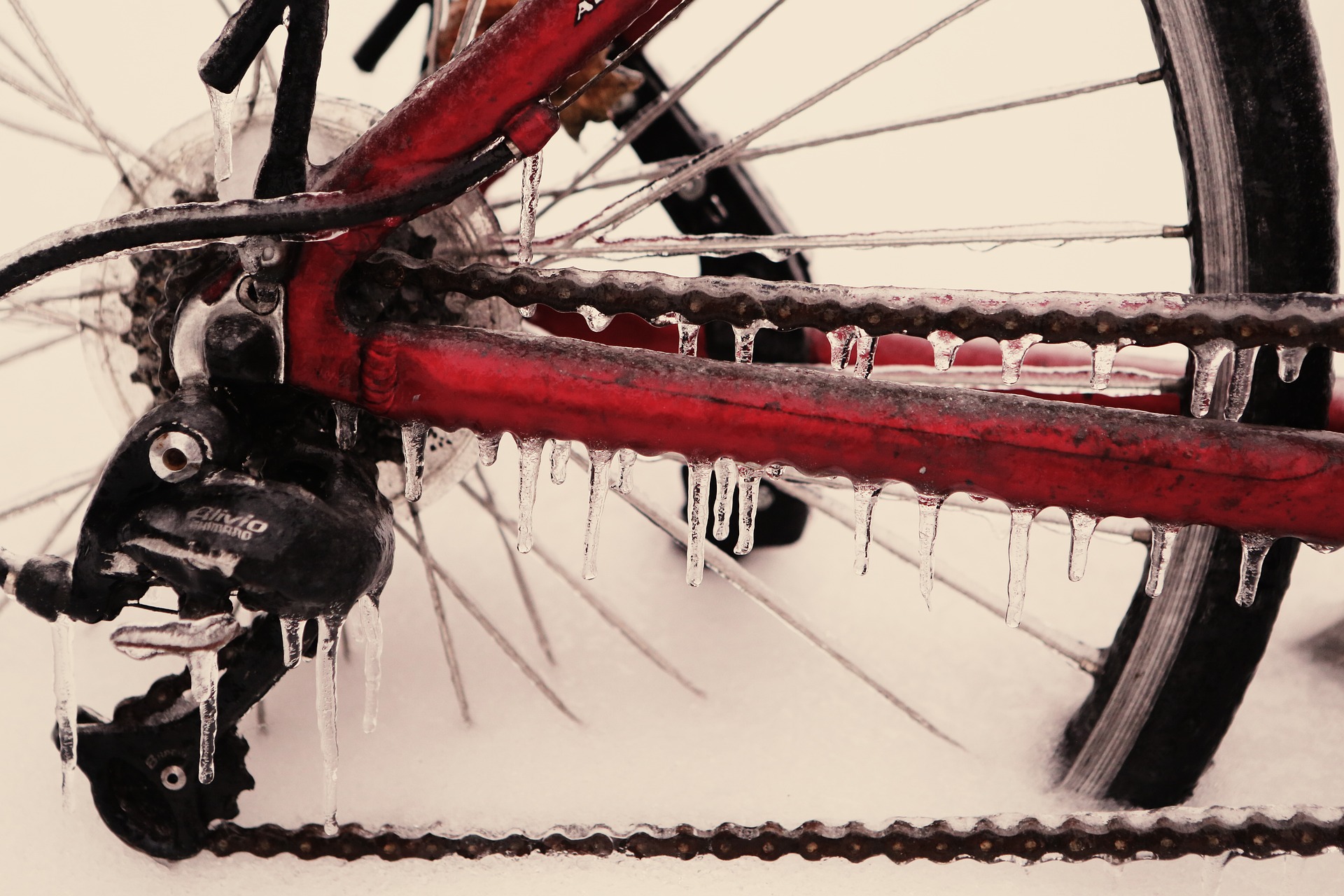 Bild von einem Fahrrad mit rotem Rahmem. Es steht im Schnee und es sind Eiszapfen an Kette, Strebe, etc.