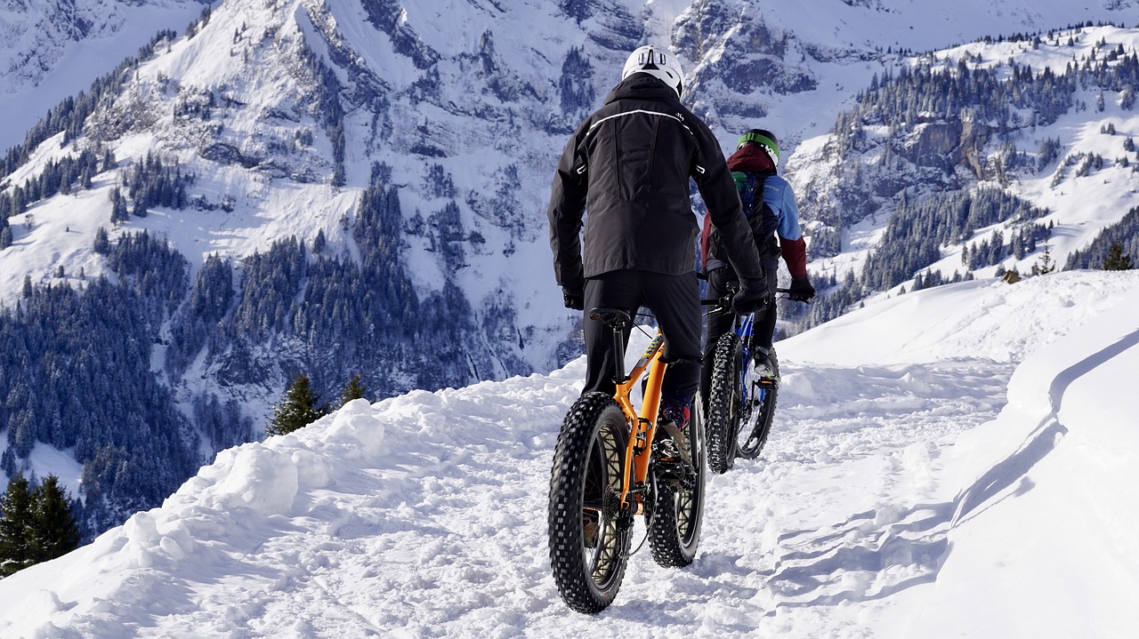 Fahrradfahrer auf einem schneebedeckten Weg, mit Fatbikes, Berge im Hintergrund